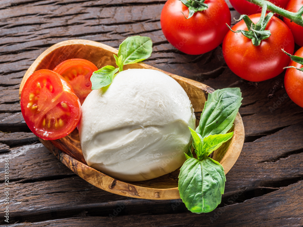 Buffalo mozzarella in the wooden bowl and cherry tomatoes on the table. Buffalo mozzarella in the wooden bowl and cherry tomatoes on the table.