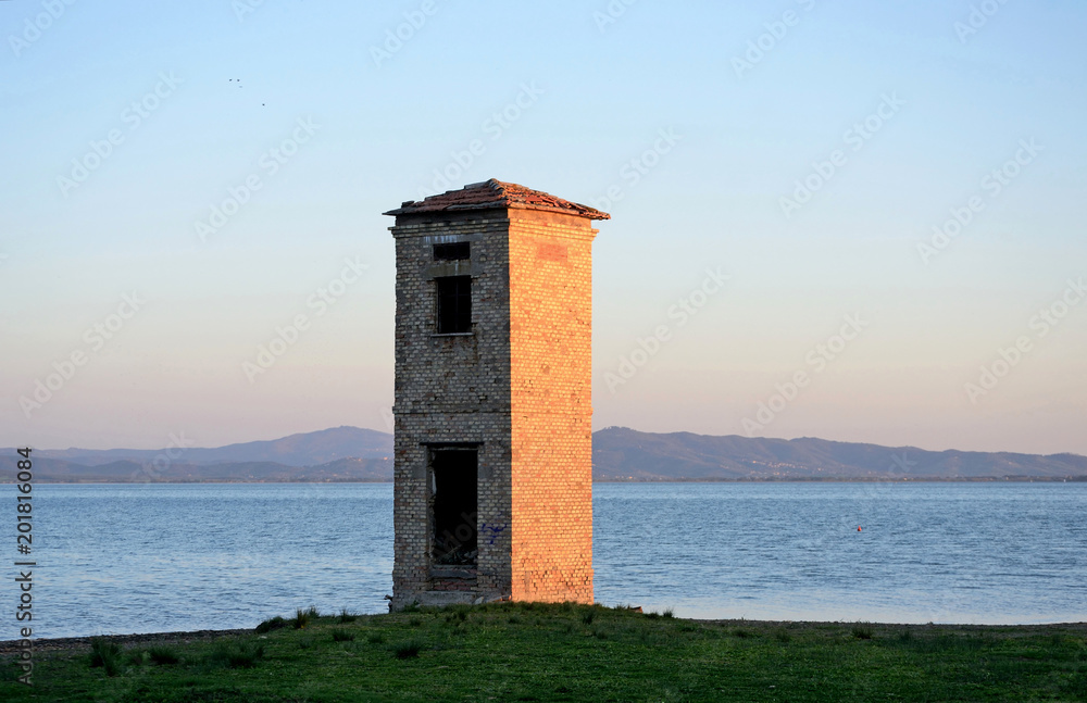 Umbria Region, Italy, old brick tower on the Lake Trasimeno shore, at sunset.  Mountain and blu sky in background