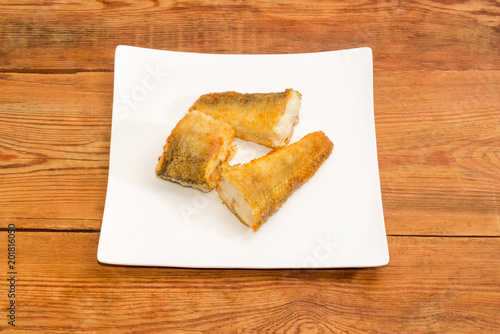 Three slices of the fried fish on a square dish photo