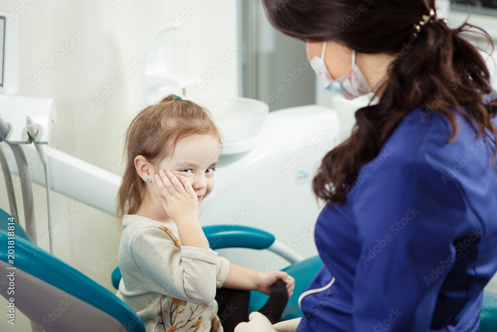 kid sits at dentist office and holds cheek