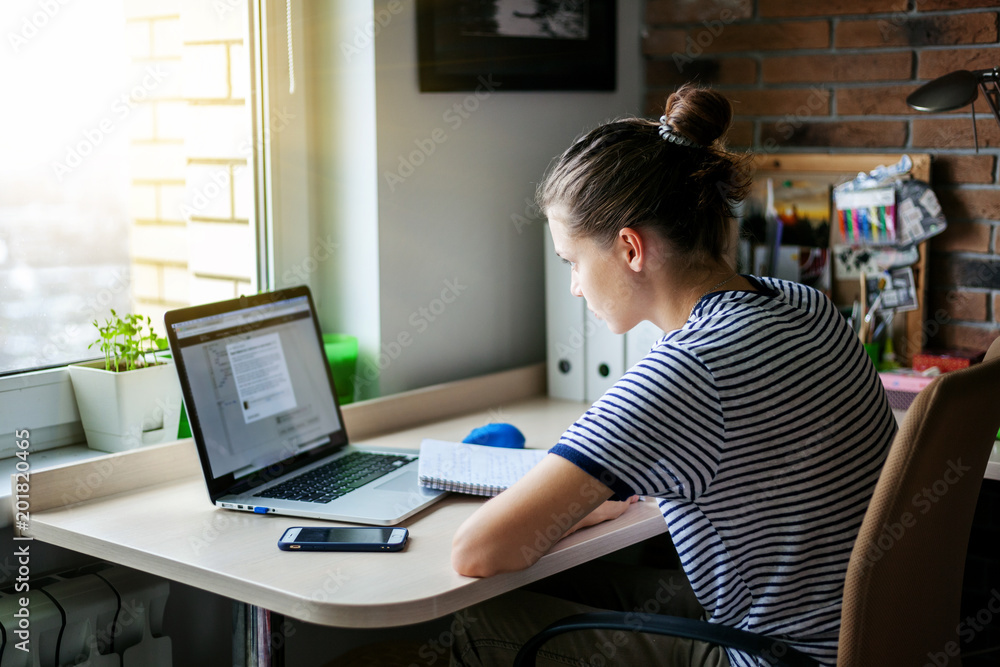 Girl student freelancer working with laptop at home by the window, education and remote work, programmer, online business