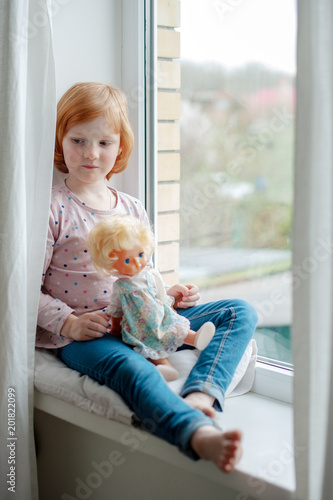 Girl playing with a doll on a windowsill