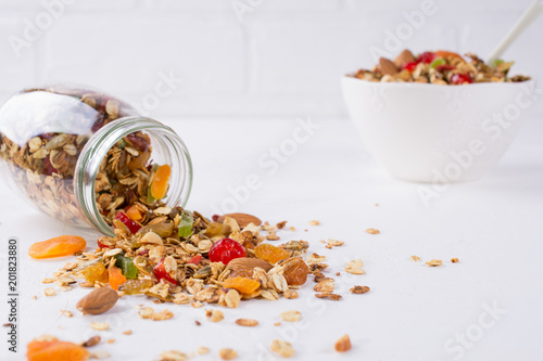 Fresh scattered granola from glass jar on white background. Copy space.