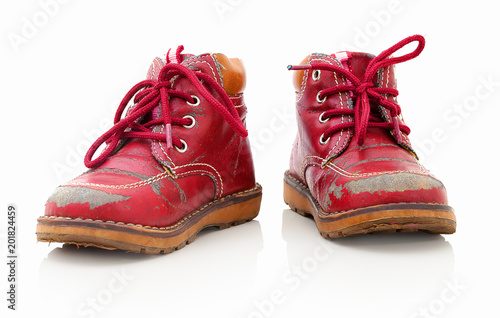 Worn out kiddie-size red lace-ups. Isolated on white background with shadow reflection. Children's shoes with laces. Small babie's booties on reflective underlay. Old ankle boots for small kid.