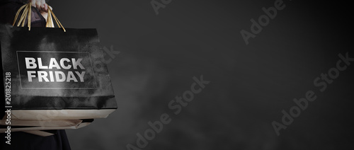 Black friday sale concept of young woman holding shopping bag on dark background with copy space fashion style