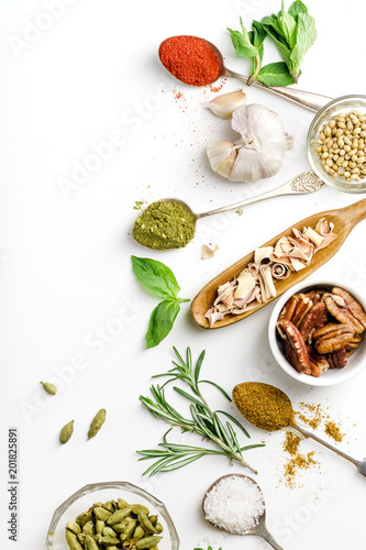Fresh herbs and dried colorful spices in spoons and bowls arranged on one side with copy space