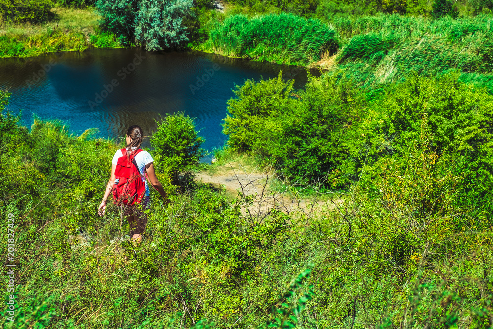 girl with a backpack, among the greenery on the shore of the lake