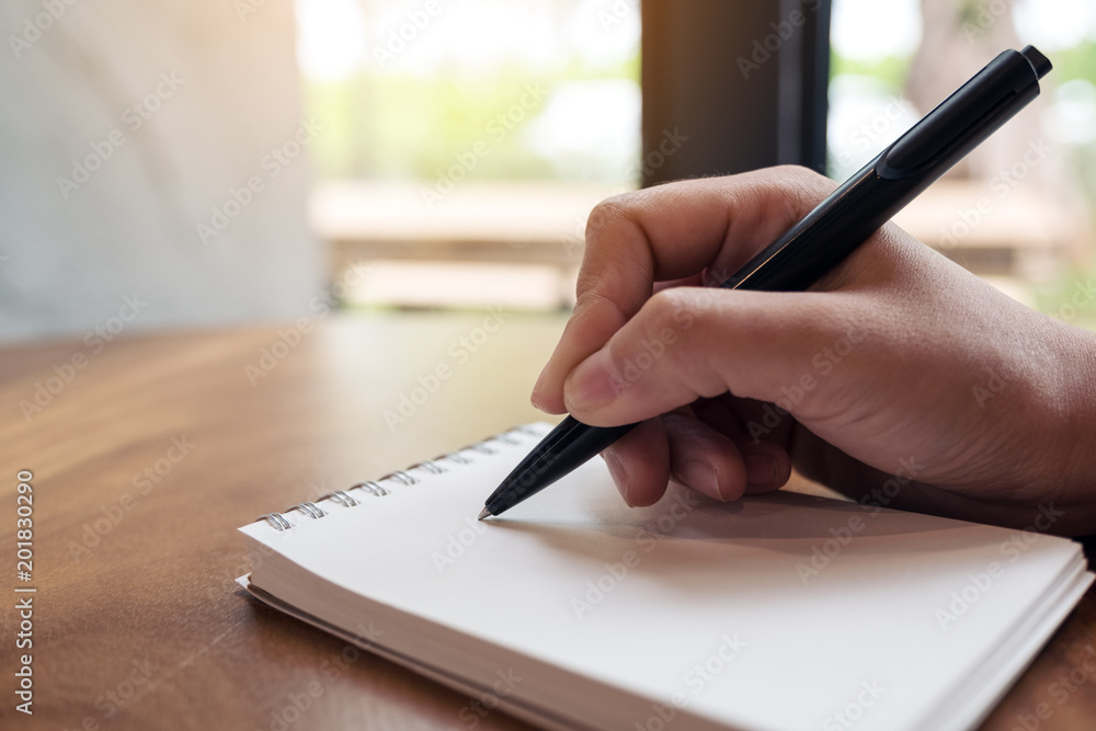 Closeup image of a woman's hands writing down on a white blank notebook on table Closeup image of a woman's hands writing down on a white blank notebook on table