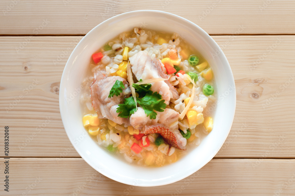 Fish and cereal porridge,top view.Fish in soft boiled cereal and rice  for breakfast on wooden table ,healthy food concept ..