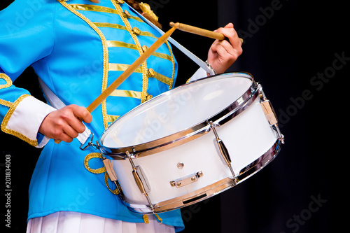 Young girl in elegant suit plays on drum. Isolated black background_