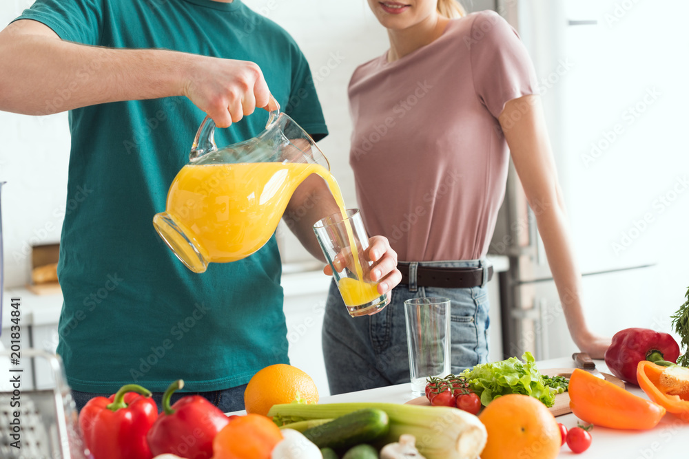 cropped image of vegan boyfriend pouring fresh juice into glass in kitchen cropped image of vegan boyfriend pouring fresh juice into glass in kitchen