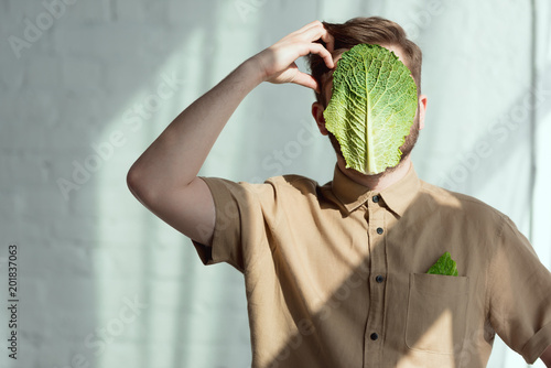 obscured view of pensive man with savoy cabbage leaf on face, vegan lifestyle concept photo