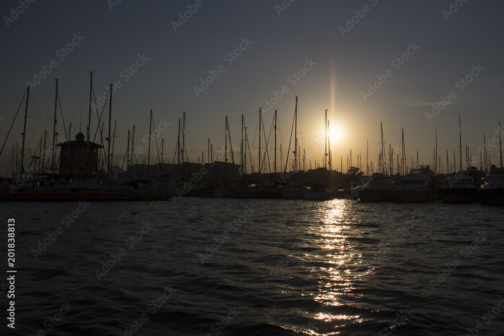 Sunset in the harbor of torrevieja with motor boats and sailing ships and the evening setting sun on the blue and orange sky