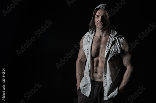 Sportsman show biceps and triceps in sleeveless shirt. Man athlete wear hood. Bodybuilder with fit torso muscles. Sport power and bodycare concept. Training activity in gym, vintage, copy space