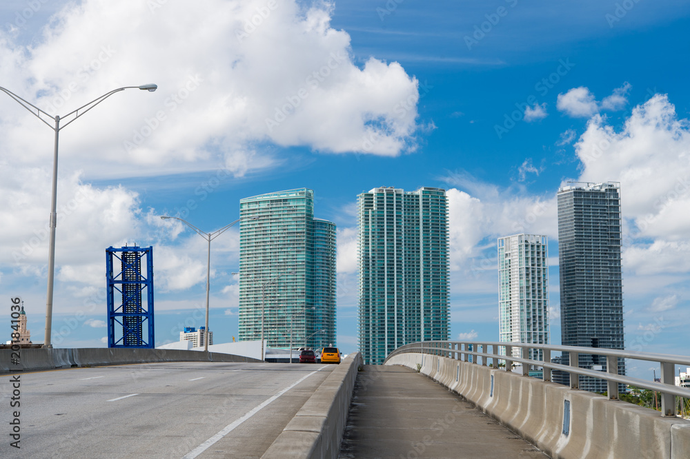 Highway with cars and skyscrapers of miami, usa. Road or roadway for transport traffic on cloudy blue sky. Public infrastructure concept. Travelling and trip by car