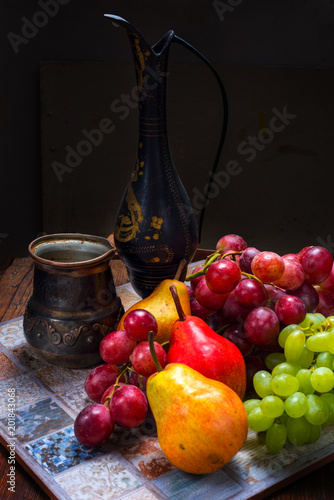Antique metal jug, grapes and pear on wooden table