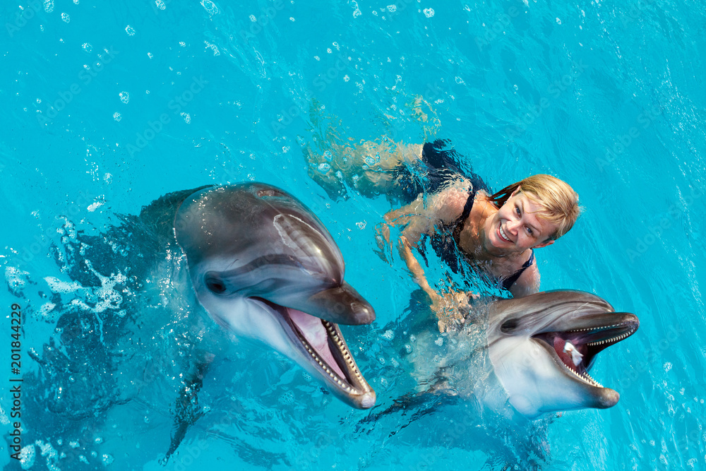 Obraz premium Trener pływa w wodzie z delfinami. Terapia wspomagana delfinami.