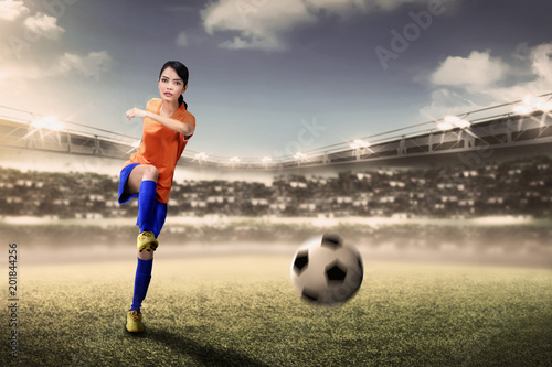 Attractive asian footballer woman kicking ball during match