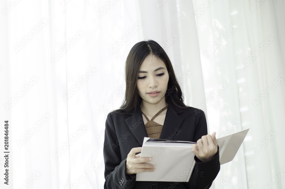 Asian women In black suit Standing holding a white book and smiling happily at work in the morning.Businesswoman standing White background,Black spots on the face of a woman caused by sunlight. Asian women In black suit Standing holding a white book and smiling happily at work in the morning.Businesswoman standing White background,Black spots on the face of a woman caused by sunlight.