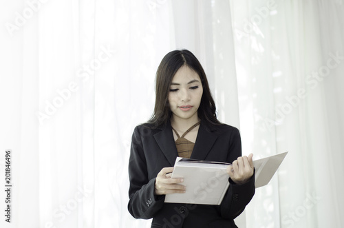 Asian women In black suit Standing holding a white book and smiling happily at work in the morning.Businesswoman standing White background,Black spots on the face of a woman caused by sunlight.