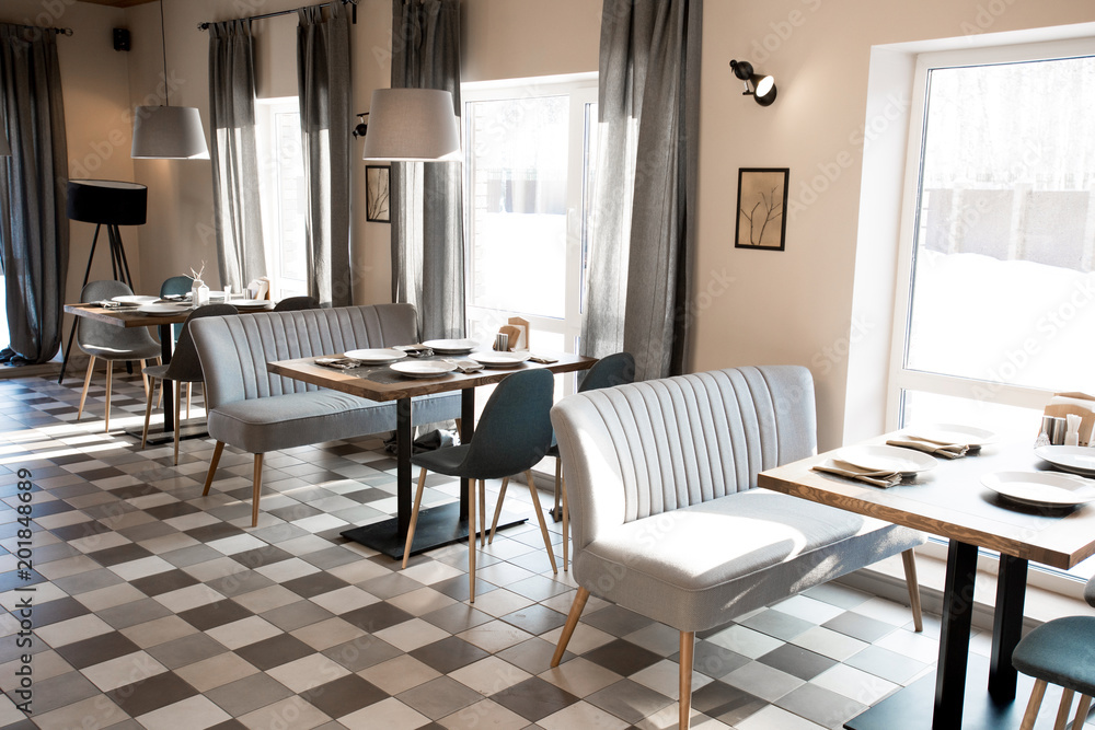 Fototapeta premium Wooden table with setting places and chairs and antique sofa around it, panoramic windows with curtains and pictures on wall