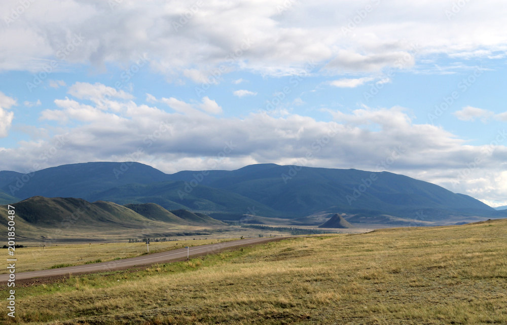 Wide steppe with yellow grass under a blue sky with white clouds Sayan mountains Siberia Russia