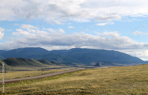 Wide steppe with yellow grass under a blue sky with white clouds Sayan mountains Siberia Russia © lkurganskaya