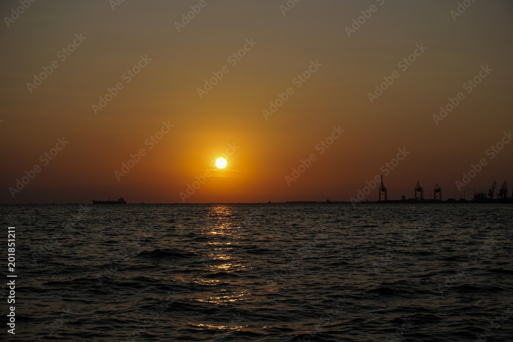 Sea level sunset with ship and port cranes landscape view.Sunset at Thessaloniki, Greece waterfront.