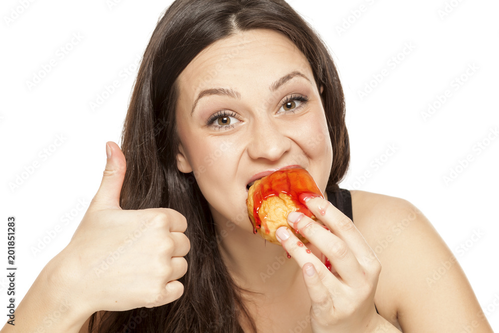 A giddy young woman eats a donut with an topping of cherry on a white background A giddy young woman eats a donut with an topping of cherry on a white background