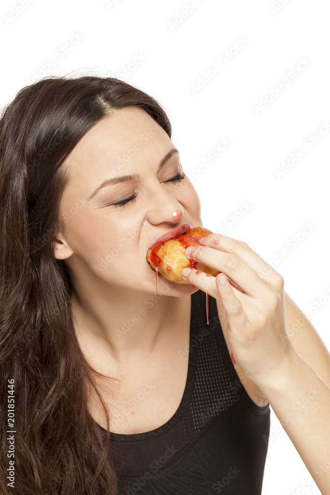 A giddy young woman eats a donut with an topping of cherry on a white background A giddy young woman eats a donut with an topping of cherry on a white background
