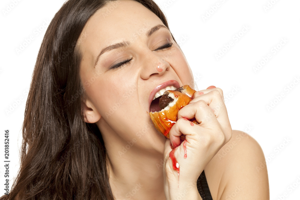 A giddy young woman eats a donut with an topping of cherry on a white background A giddy young woman eats a donut with an topping of cherry on a white background