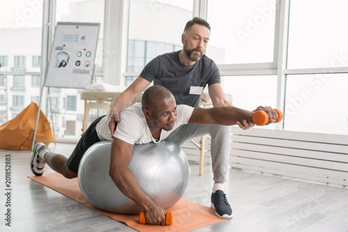 Rehabilitation exercises. Nice pleasant hard working man lying on the medball while having a workout photo