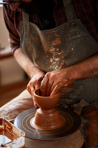 Portrait of a male potter in apron molds bowl from clay, selective focus, close-up photo