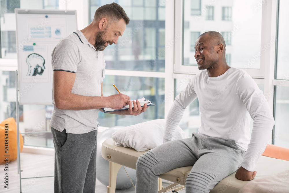 Obraz premium Appointment with a therapist. Pleasant bearded doctor listening to his patient and taking notes