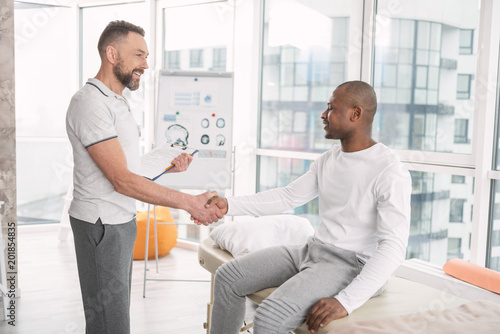 Nice to see you. Joyful positive delighted doctor looking at his patient while shaking his hand