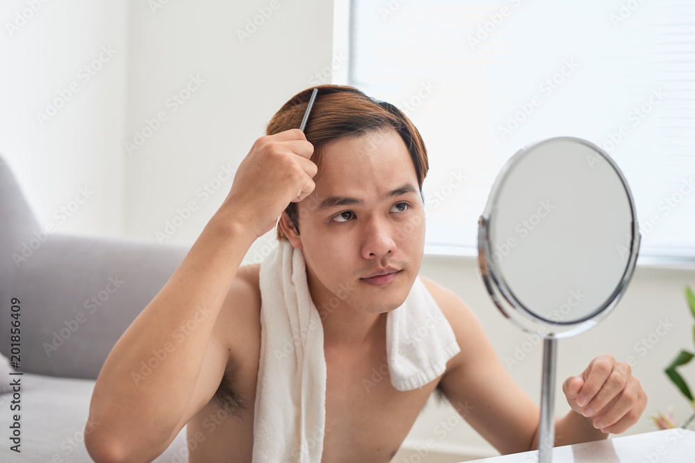 Portrait of handsome man looking at himself in mirror and brushing his hair. Portrait of handsome man looking at himself in mirror and brushing his hair.