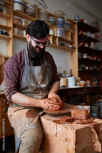 Portrait of a male potter in apron molds bowl from clay, selective focus, close-up photo