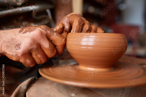 Close-up hands of a male potter in apron making a vase from clay, selective focus
