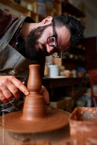 Portrait of a male potter in apron molds bowl from clay, selective focus, close-up photo