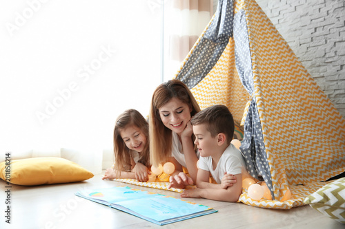 Photos Nanny and little children reading book in tent at home