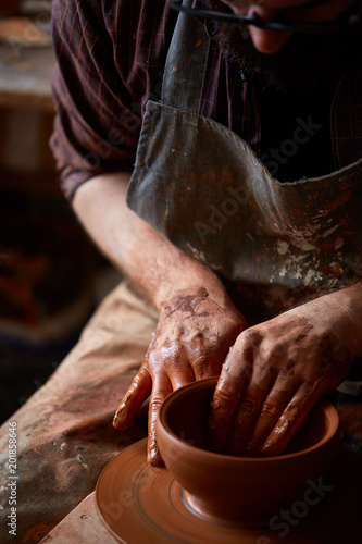 Portrait of a male potter in apron molds bowl from clay, selective focus, close-up photo