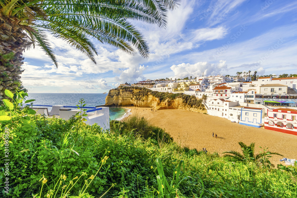 Sandy beach surrounded by cliffs with palm trees in Carvoeiro, Algarve, Portugal