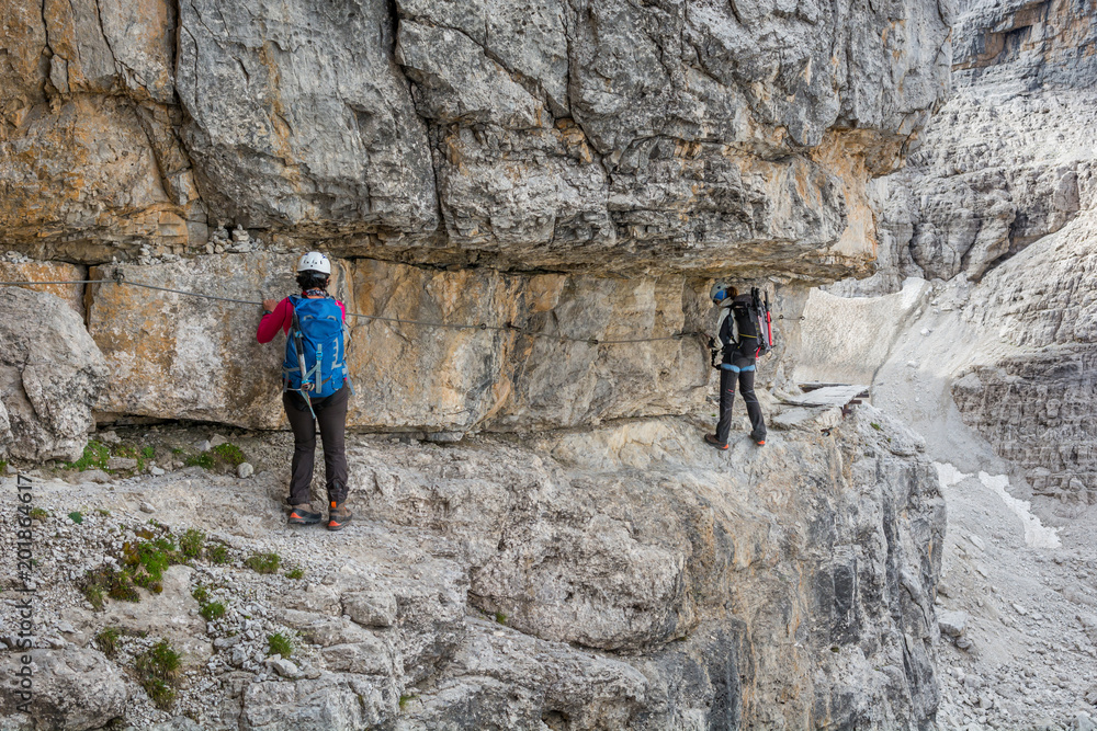 Climbers walking on narrow ledge protected by via ferrata set.