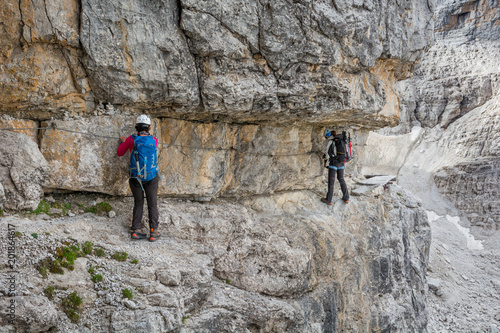 Climbers walking on narrow ledge protected by via ferrata set.