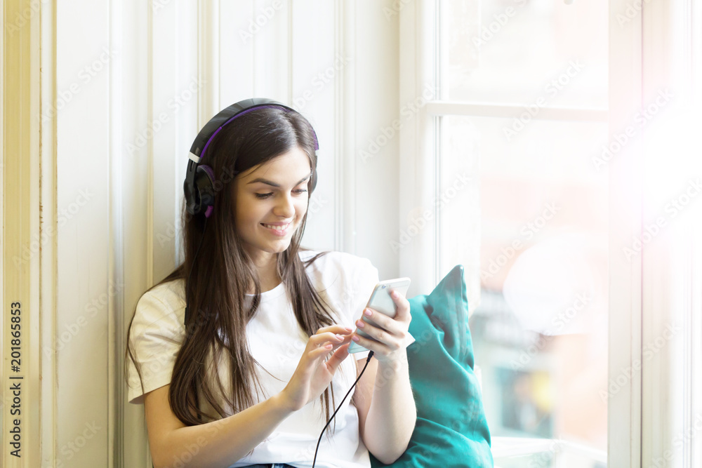 Long hair sexy girl wears headphones and white t-shirt listen to music sitting on wide windowsill Long hair sexy girl wears headphones and white t-shirt listen to music sitting on wide windowsill