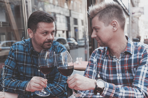gay couple toasting with red wine in a wine shop in city environemt. their look each other deep into their eyes. photo