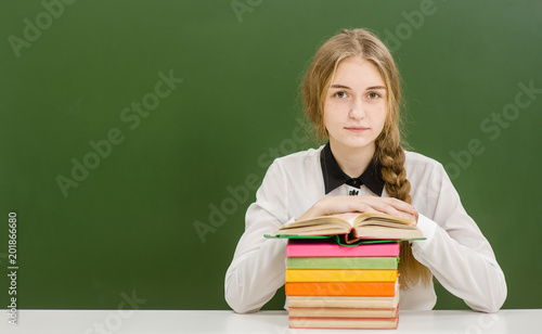 Teen girl with books on the background of a school board. Space for text