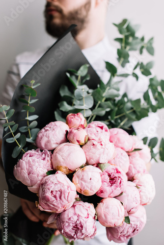 Young man with a beard holding a beautiful blossoming fragrant mono bouquet of pink peonies and eucalyptus