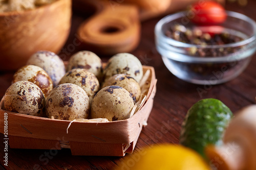 Fresh eggs of a quail with greens and vegetables on wooden table, selective focus, close-up photo