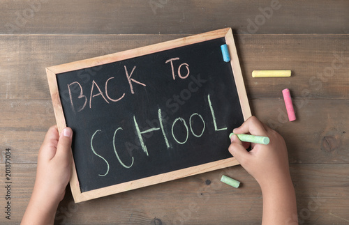 Little hand writing back to school on black chalk board